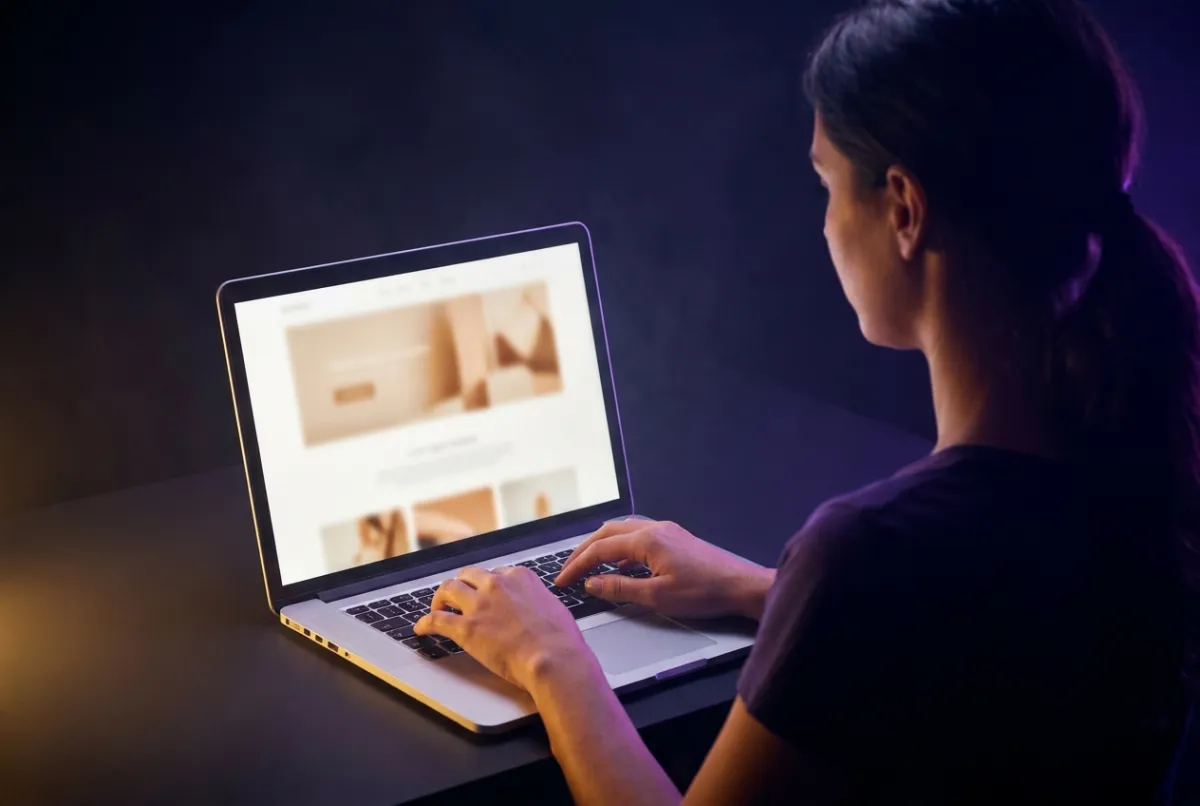 Par-dessus l’épaule d’une femme qui tape pendant qu’un site d’une page prend forme à l’écran